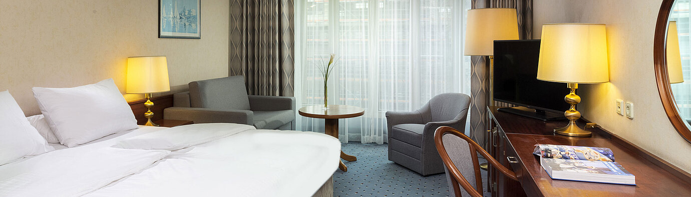 Helles Familienzimmer im Maritim Hotel Köln mit Doppelbett, Schreibtisch, Fernseher,Sesseln und großen Fenstern mit Vorhängen