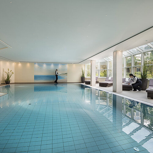 Großer Innenpool im Maritim Hotel Würzburg mit Glasfront, Liegen und freundlichem Service.