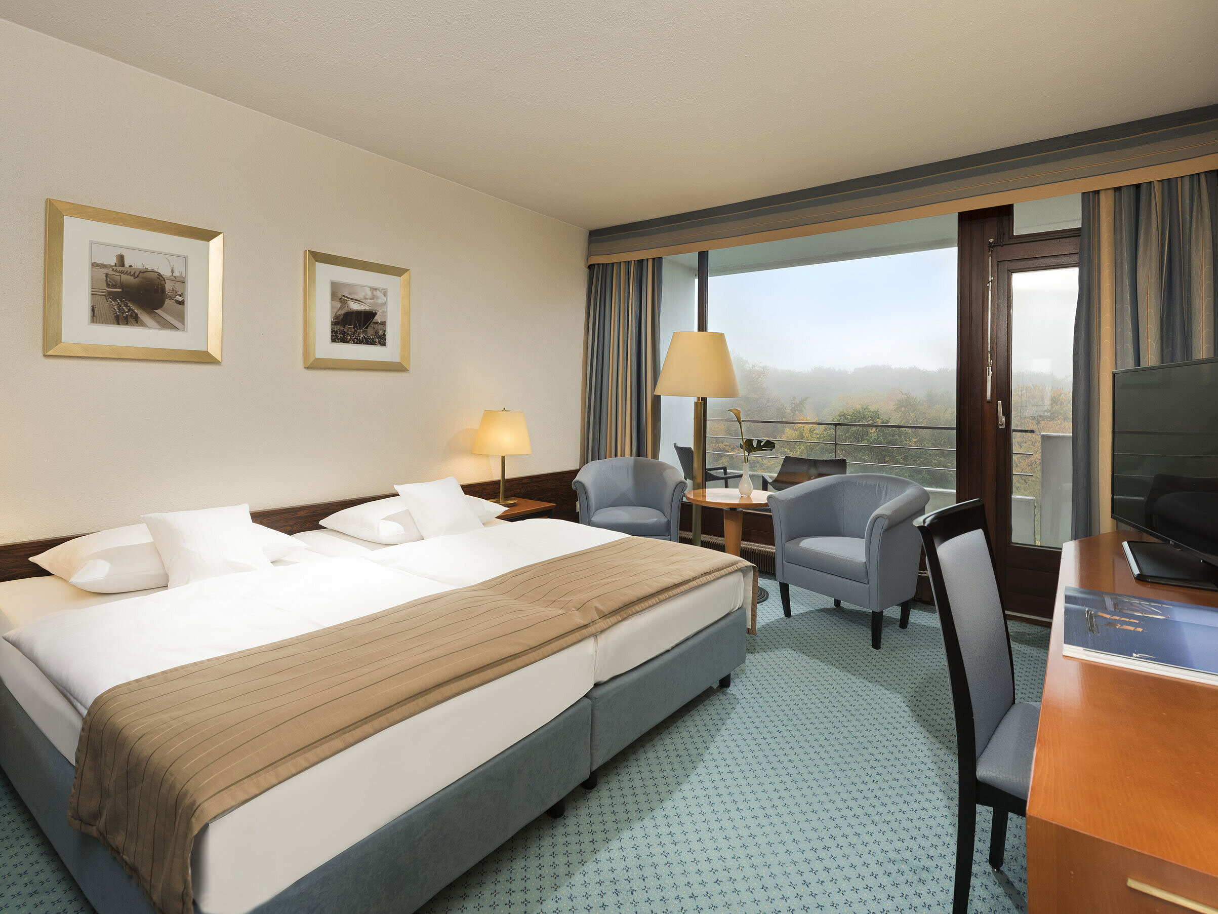 Classic Zimmer im Maritim Hotel Kiel mit großem Doppelbett, Sitzbereich, Schreibtisch und Balkon mit Blick ins Grüne.