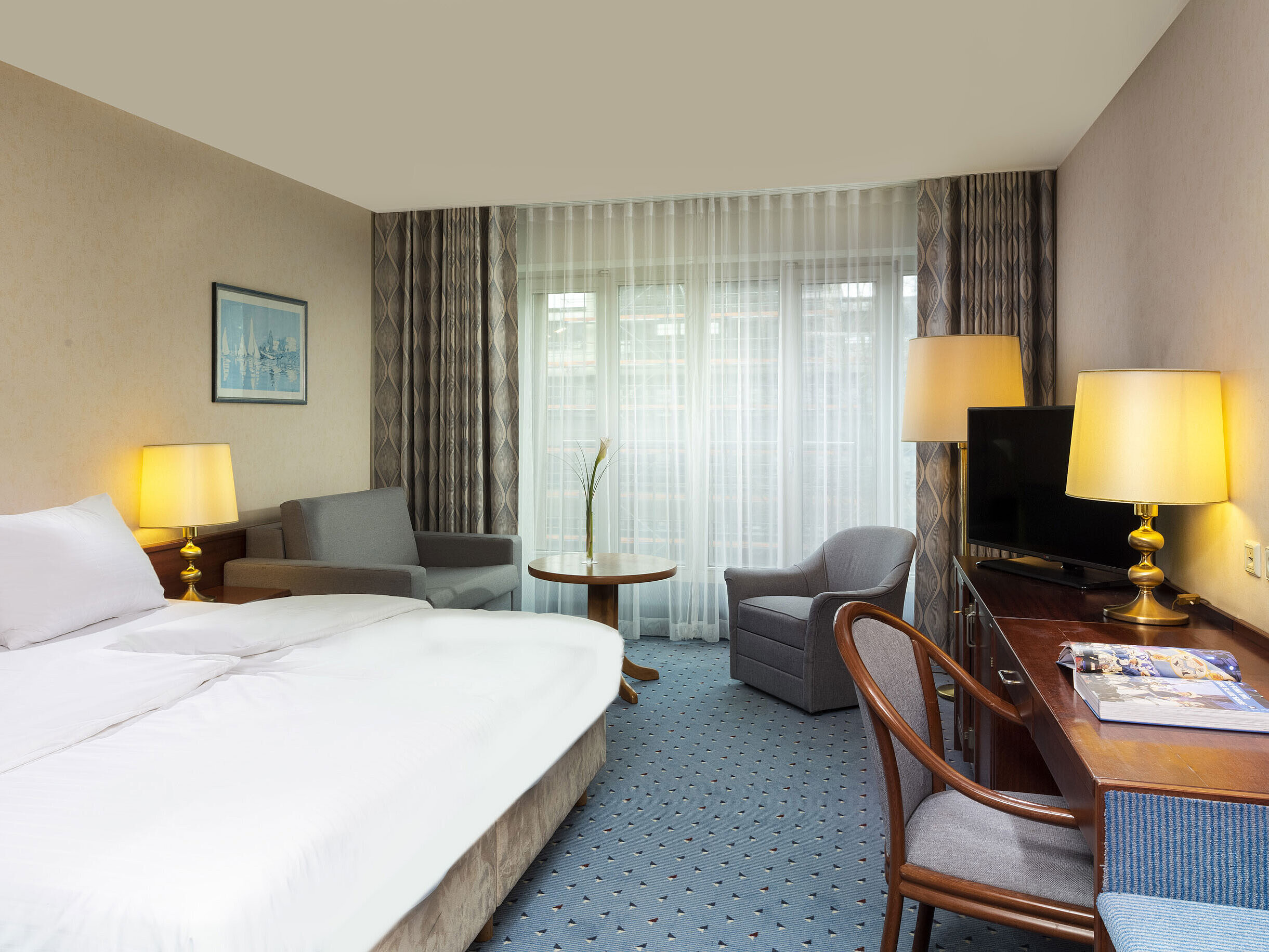 Comfort Zimmer im Maritim Hotel Köln mit Doppelbett, Schreibtisch, Sofa und modernem Interieur mit großen Fenstern.