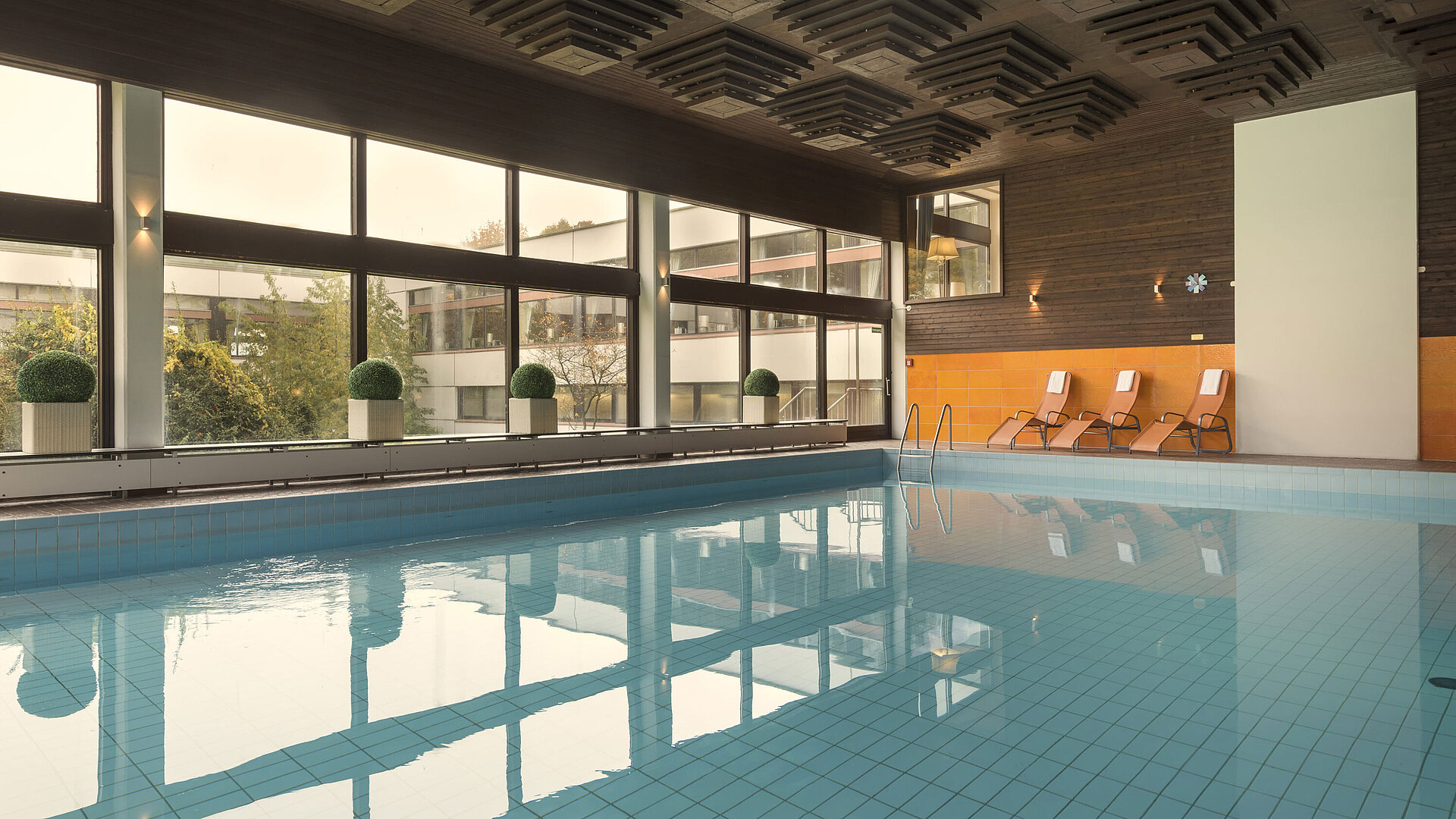 Das Bild zeigt den Innenpool des Maritim Hotels Kiel, umgeben von großen Fenstern, mit Liegestühlen für Entspannung.