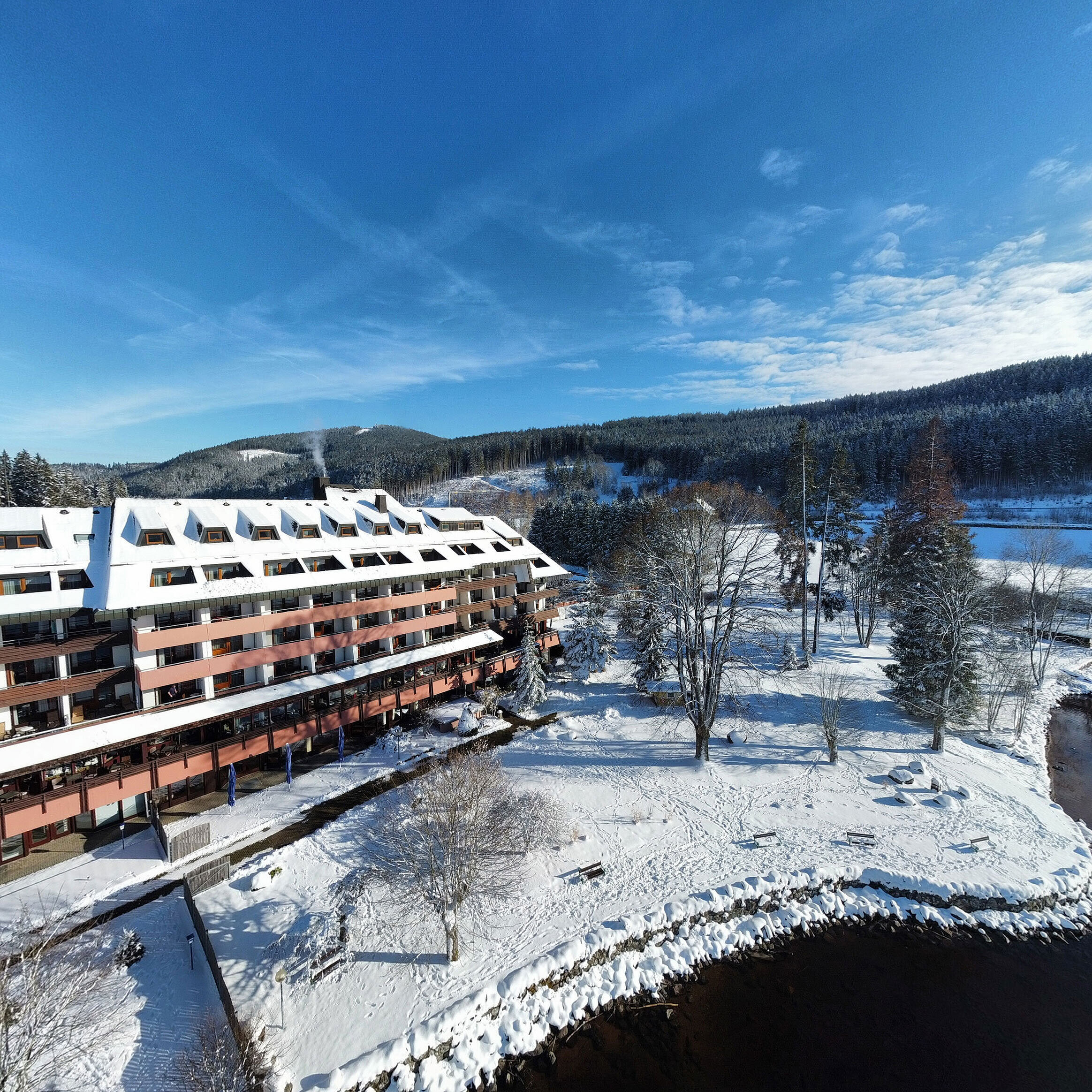 Maritim Hotel Titisee im Winter mit verschneitem Garten und Blick auf das Hotelgebäude am Ufer
