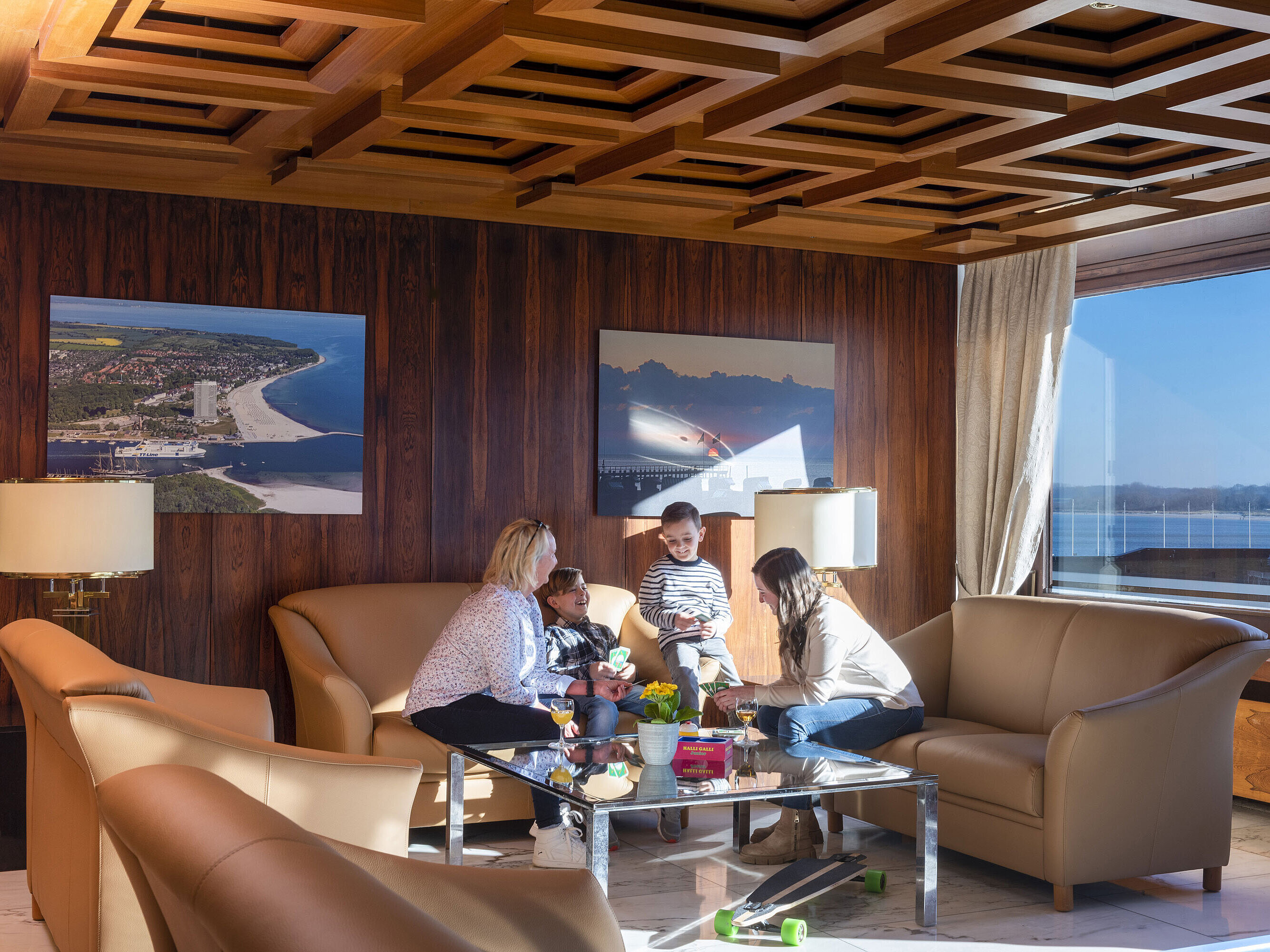 Zwei Erwachsene und zwei Kinder entspannen in der Lounge mit Blick auf die Ostsee im Maritim Hotel Travemünde