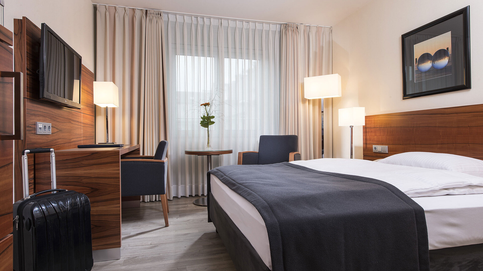 Gemütliches Zimmer mit Doppelbett, Schreibtisch und Koffer im Maritim Hotel München