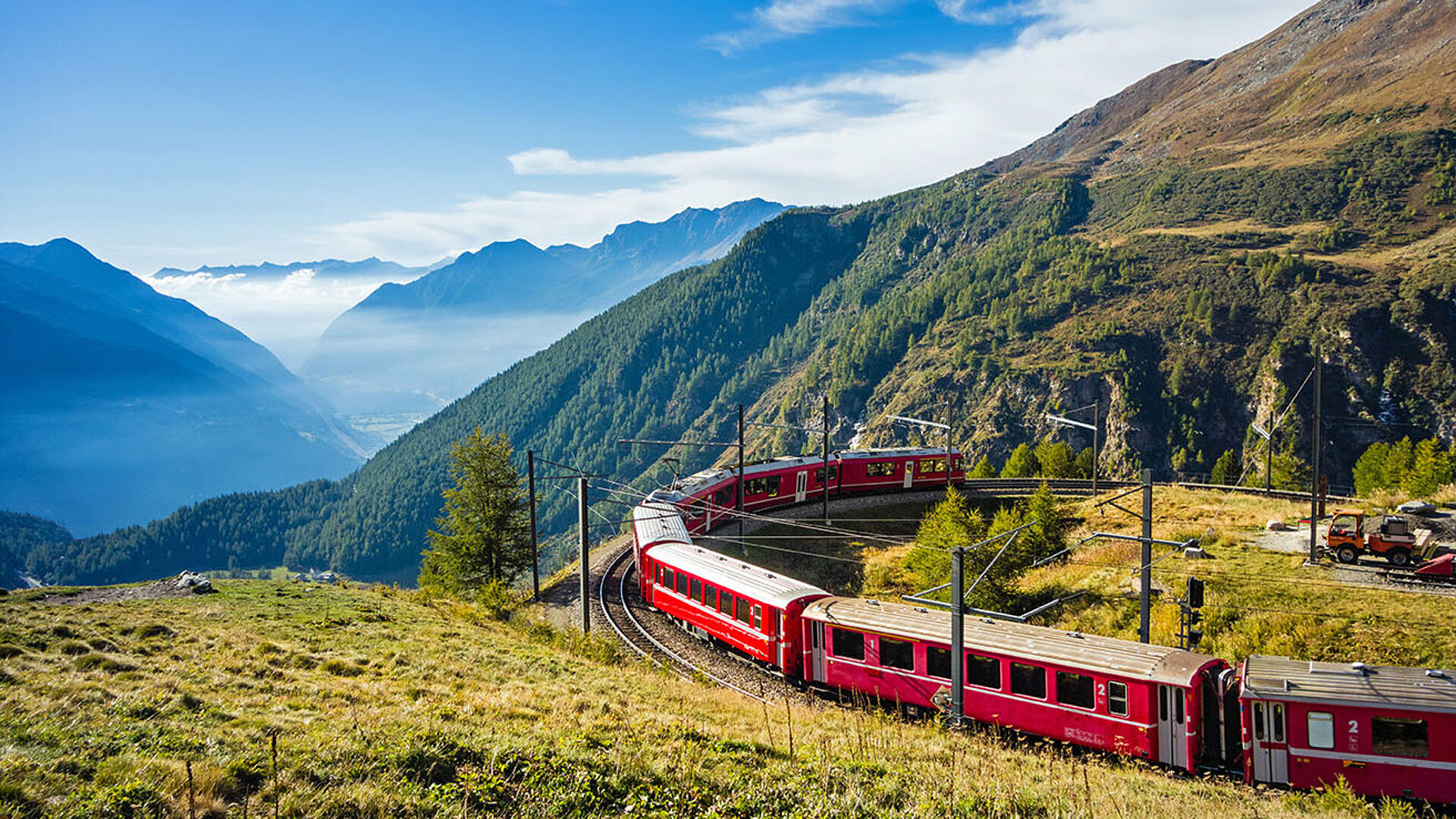 _matho_Adobestock.com.jpg Roter Zug fährt durch die Alpenlandschaft in Graubünden mit Blick auf grüne Täler und majestätische Berge