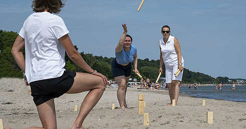 Schwedenschach Drei Personen spielen Wikingerschach am Strand vor dem Maritim Seehotel Timmendorfer Strand bei sonnigem Wetter.