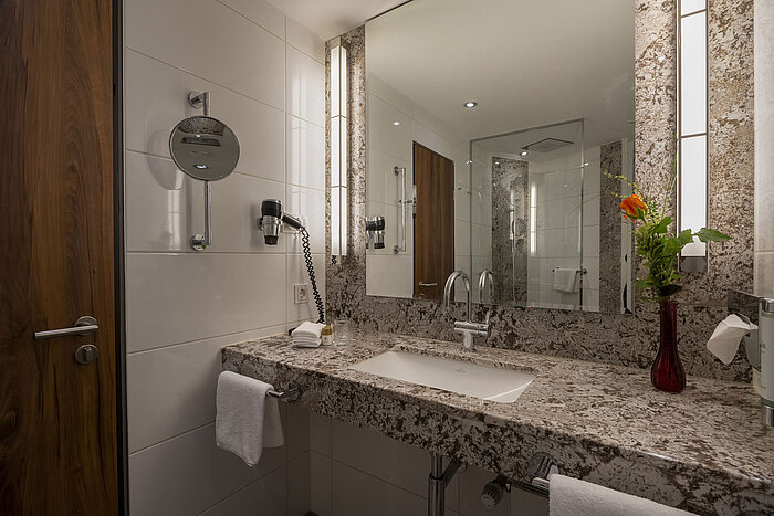 Modernes Badezimmer im Maritim Hotel Bad Homburg mit Granitwaschtisch, Spiegel und stilvoller Beleuchtung.