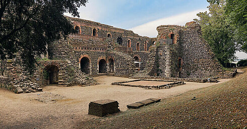 Historische Burgruine aus Naturstein mit Innenhof und Bäumen in sonniger Landschaft
