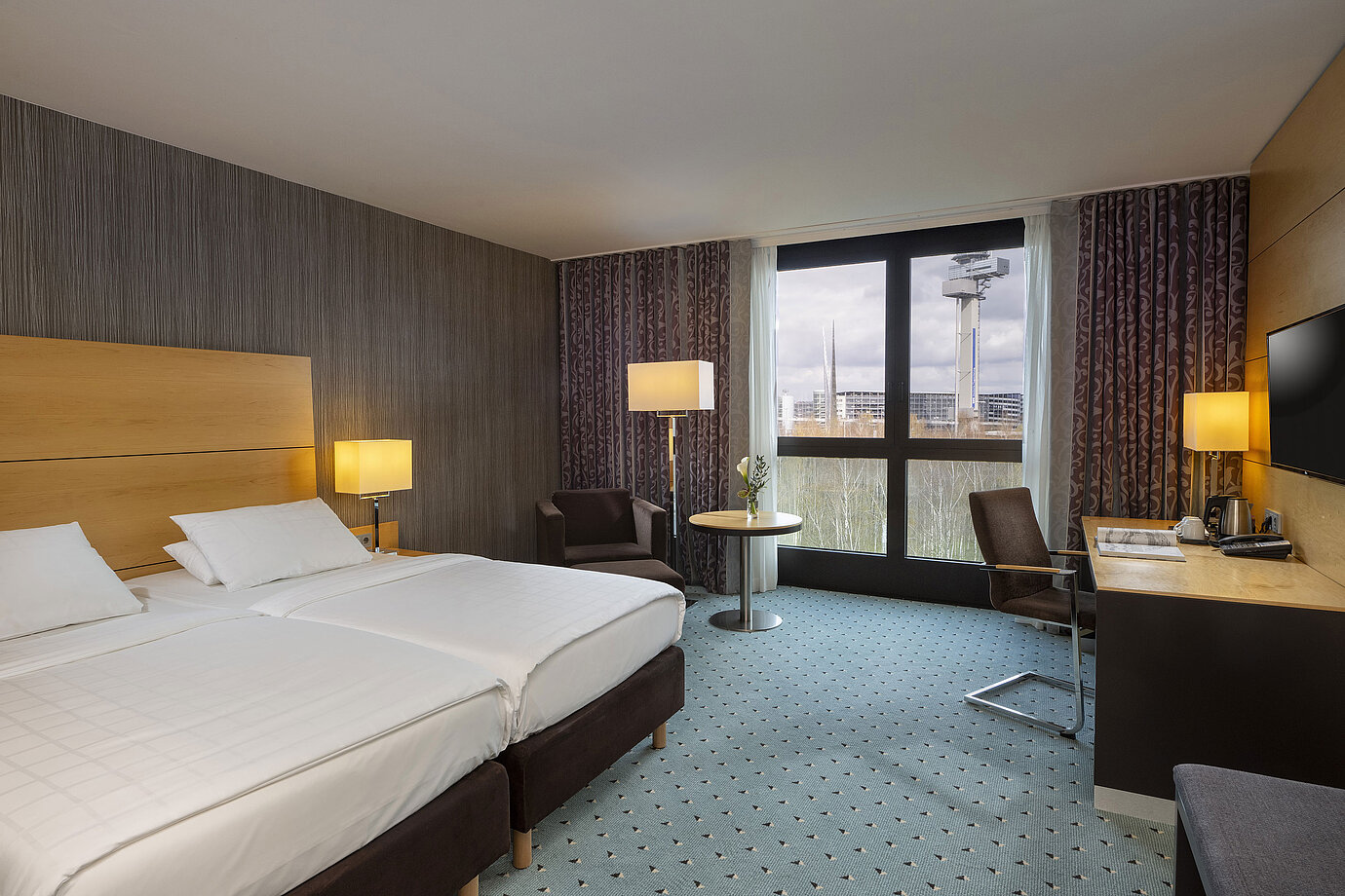 Classic Zimmer im Maritim Hotel Düsseldorf mit Doppelbett, Schreibtisch und Panoramafenster mit Blick auf die Umgebung.