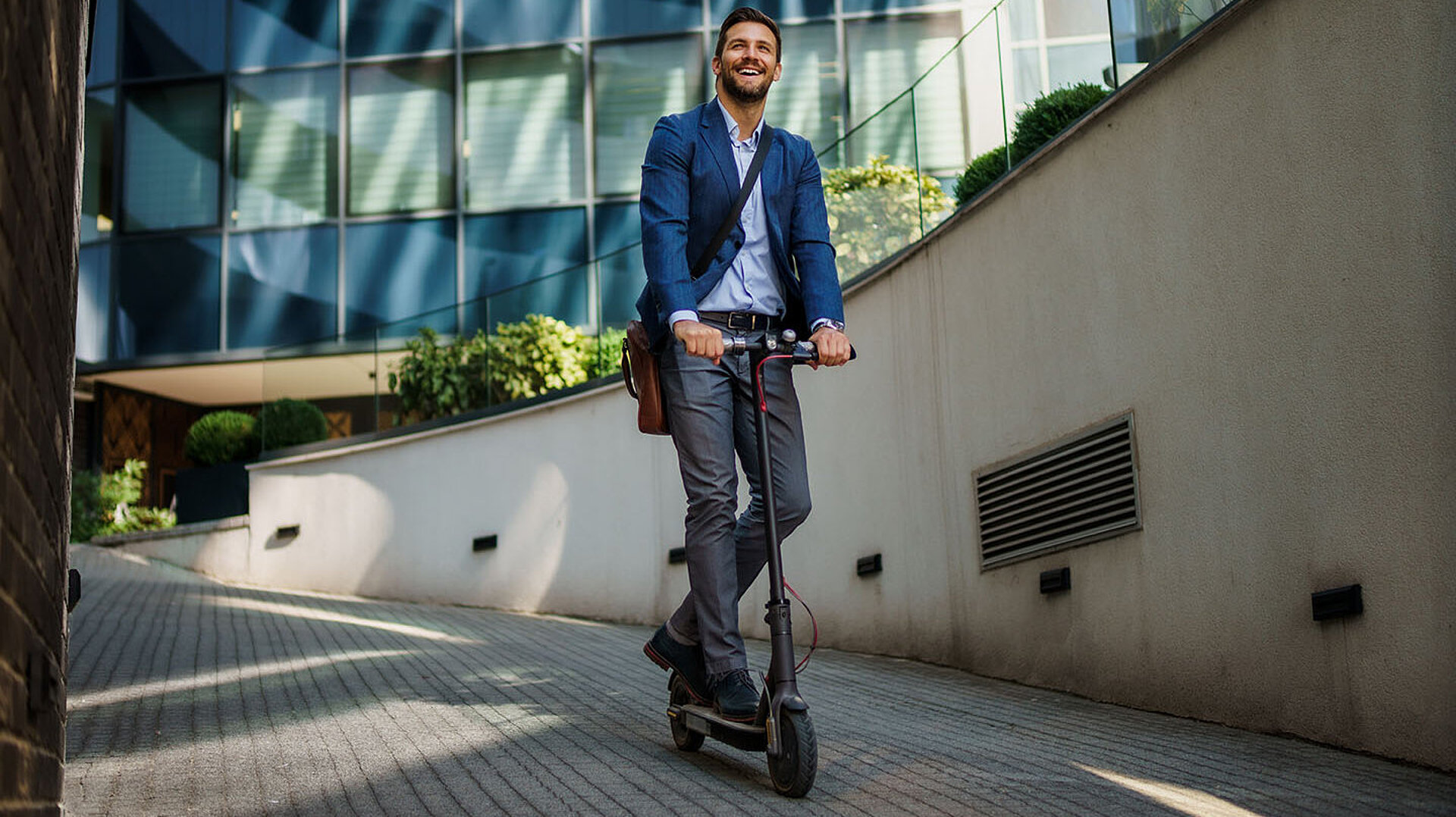 Mann fährt mit einem E-Scooter auf einem Weg in einer modernen Stadtumgebung.