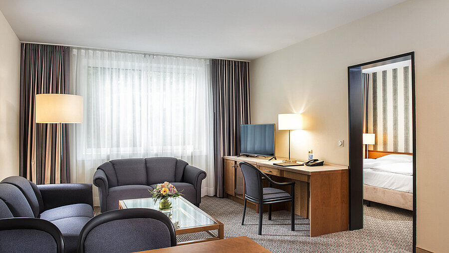 Wohnbereich mit Sofas, TV, Schreibtisch und Blick ins Schlafzimmer im Maritim Hotel Stuttgart
