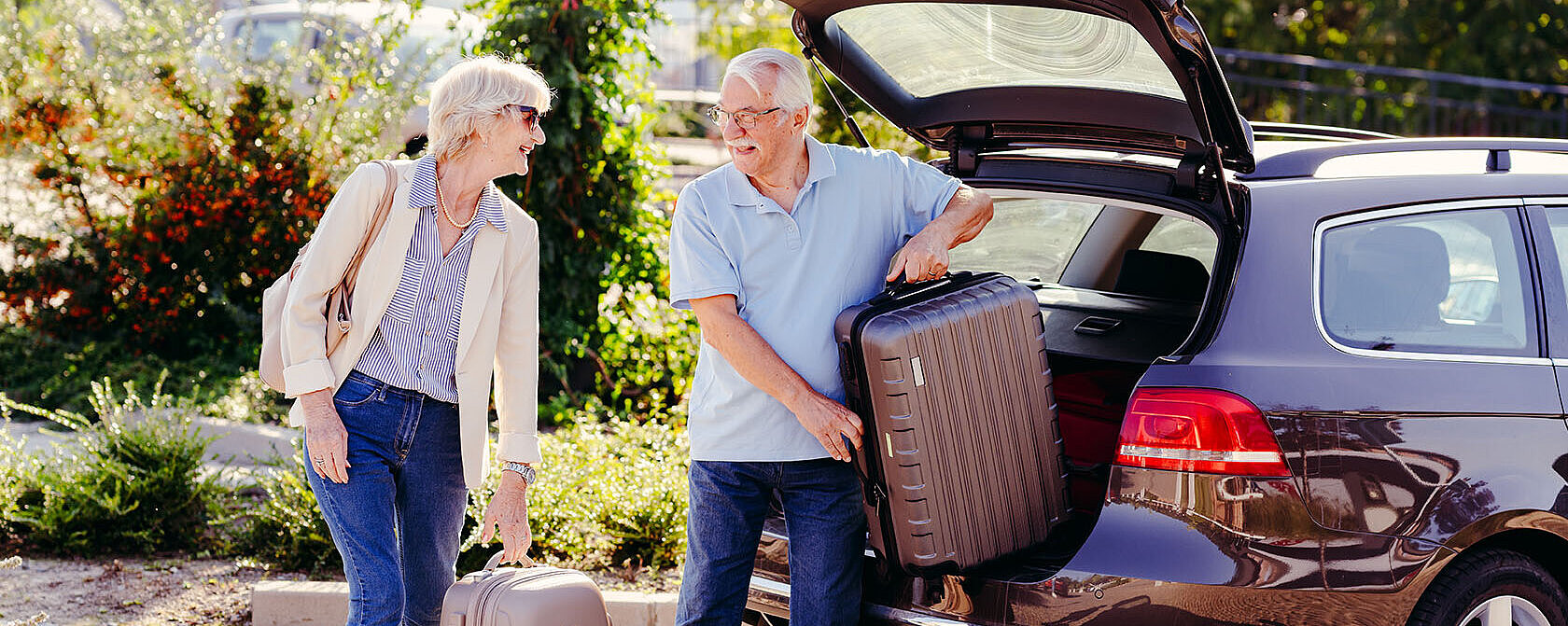 Älteres Paar lädt Koffer aus dem Kofferraum eines Autos und bereitet sich auf eine Reise vor.