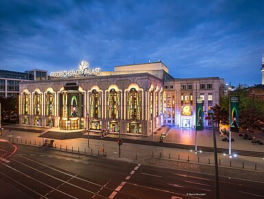 Beleuchteter Friedrichstadt-Palast in Berlin bei Abenddämmerung mit Fernsehturm im Hintergrund