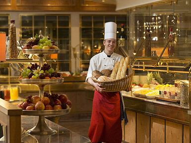 Bäcker mit Brotkorb am Frühstücksbuffet des Maritim Hotel Stuttgart, umgeben von frischem Obst