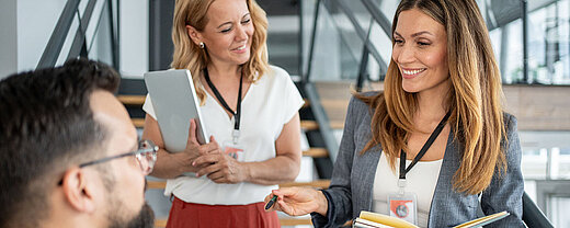 Drei Geschäftsleute mit Notizbüchern im Gespräch bei einem Networking-Event
