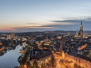 Nachtpanorama von Ulm mit beleuchtetem Münster und Donau, stimmungsvoll zur blauen Stunde.