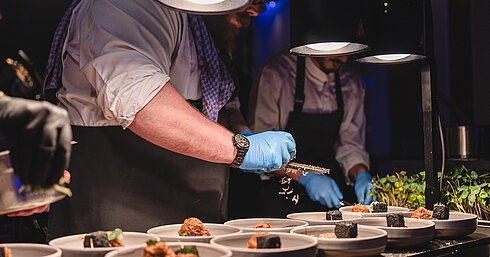 Live-Cooking bei einer Veranstaltung © Thomas Loris Koch richtet bei einer Live-Cooking-Station mehrere Gerichte frisch an und präsentiert kulinarische Spezialitäten.