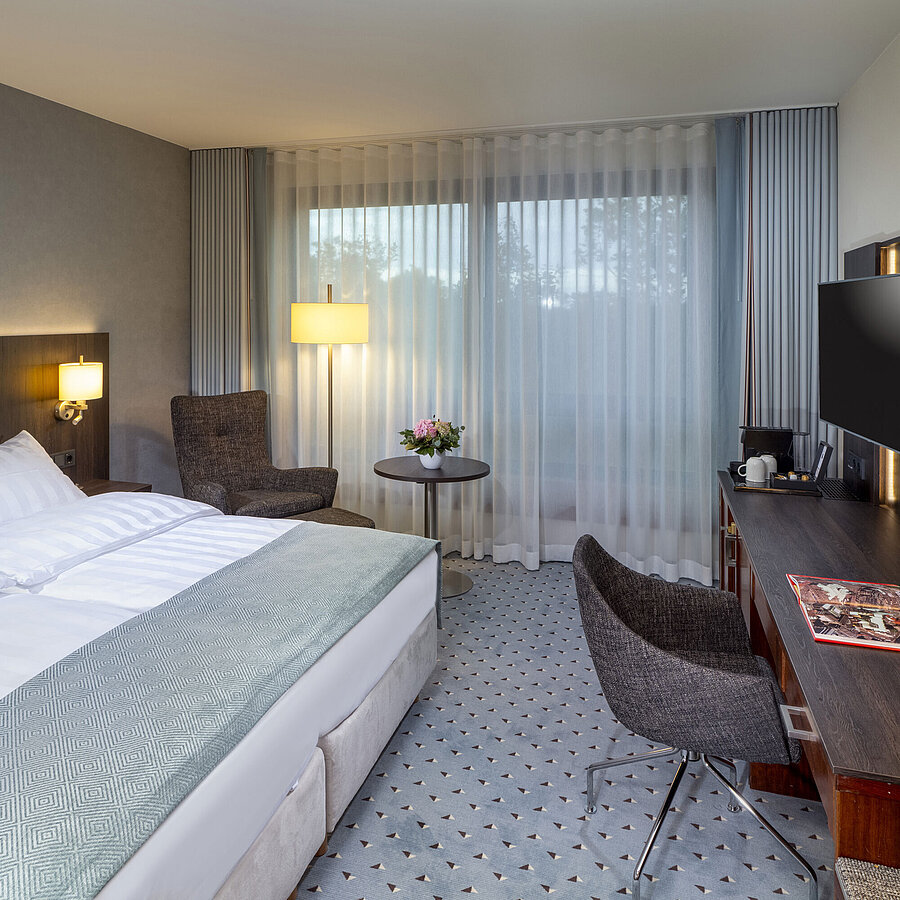 Modernes Superior Doppelzimmer im Maritim Bremen mit Sitzbereich, Schreibtisch und großem Fenster für natürliche Beleuchtung.