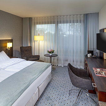 Modernes Superior Doppelzimmer im Maritim Bremen mit Sitzbereich, Schreibtisch und großem Fenster für natürliche Beleuchtung.