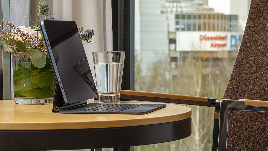 Detailaufnahme eines Tisches im Maritim Hotel Düsseldorf mit Tablet, Glas Wasser und Blick auf den Flughafen Düsseldorf.