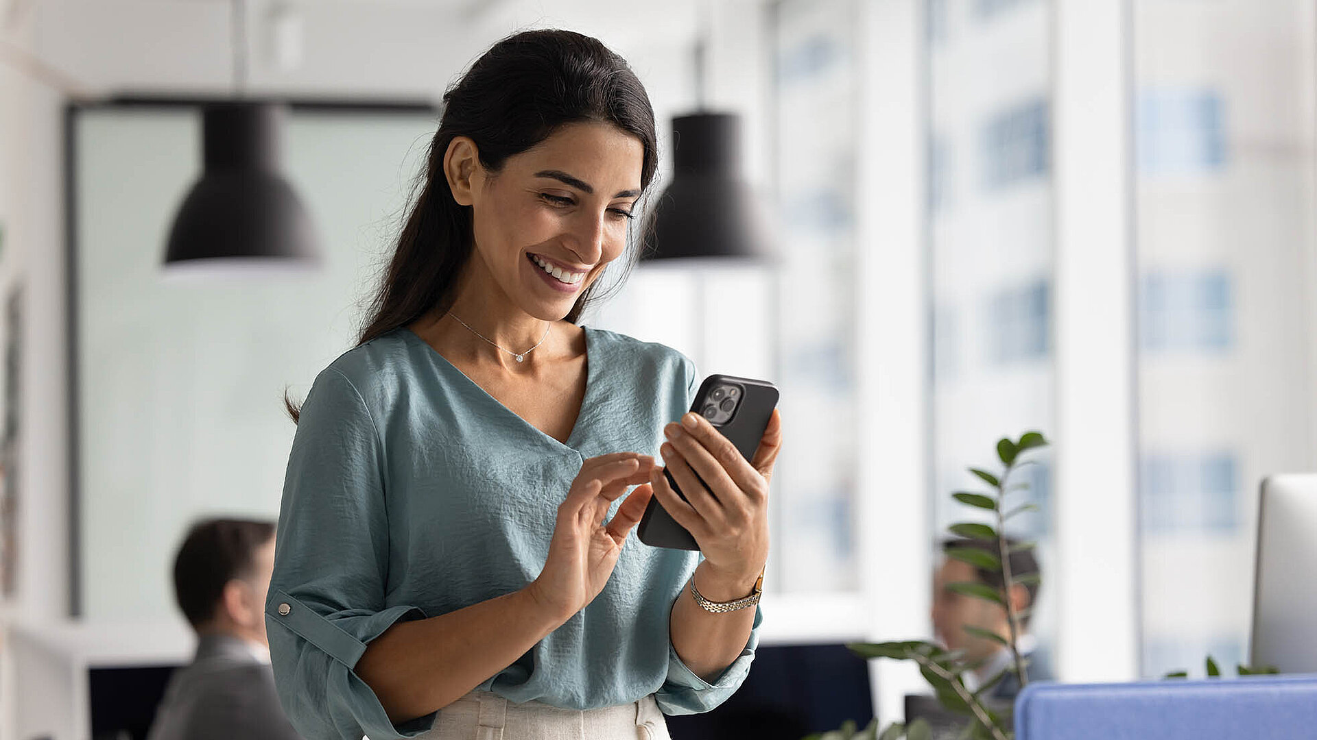 Geschäftsfrau im modernen Büro lächelt beim Blick auf ihr Smartphone.