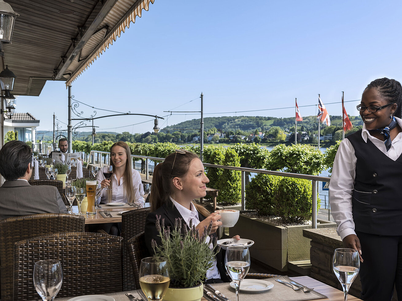 Gäste genießen Kaffee und Wein auf der Terrasse des Maritim Hotel Königswinter mit malerischem Blick auf den Rhein.
