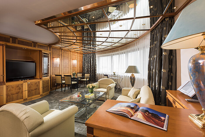 Blick in die luxuriöse Suite mit gemütlicher Sitzecke, TV und dekorativem Decken-Design im Maritim Hotel Magdeburg