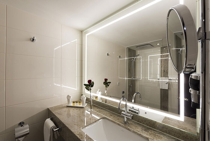 Modernes Bad im Maritim Hotel Würzburg mit großem beleuchtetem Spiegel und edler Granitplatte.