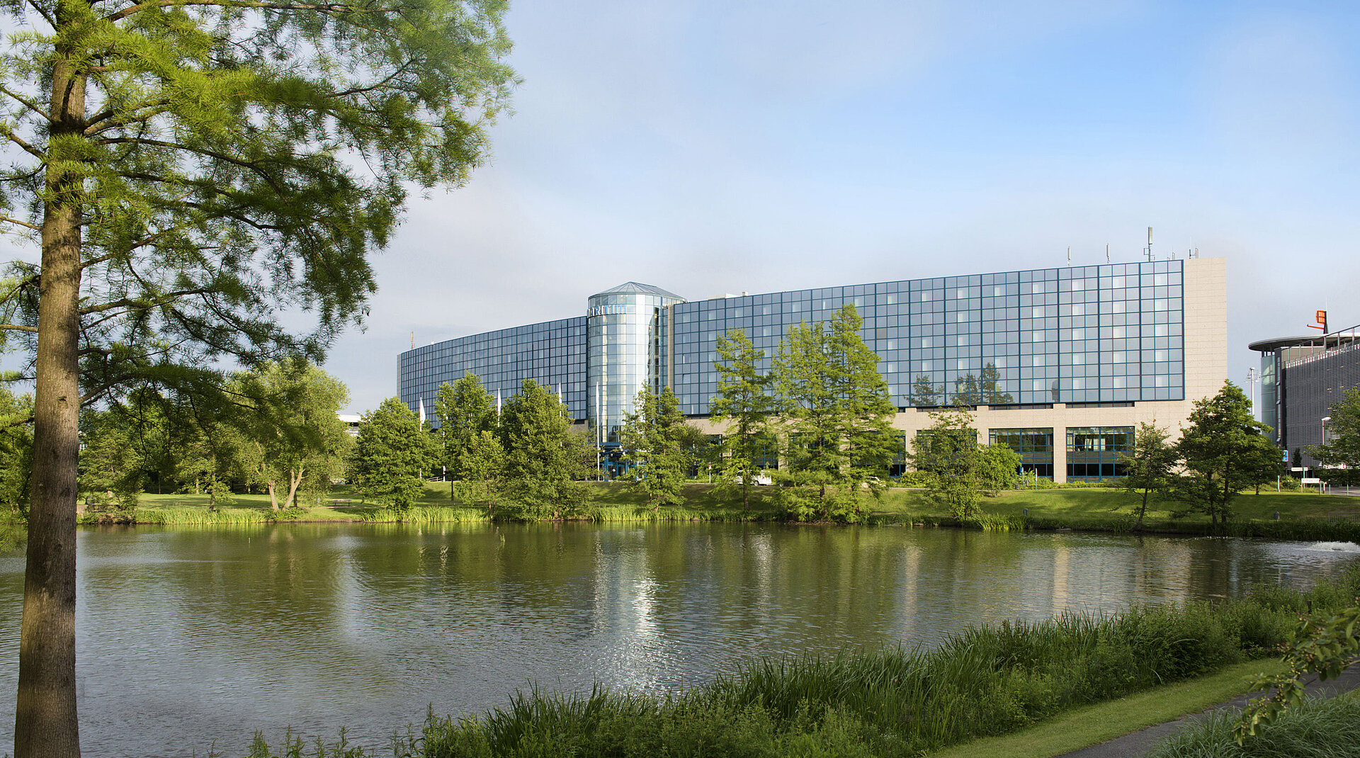 Das moderne Maritim Hotel Hannover mit Glasfassade und Blick auf den See inmitten einer grünen Landschaft.