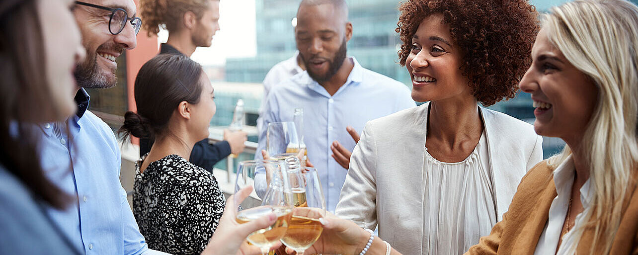Kolleg:innen stoßen bei einem Business-Event mit Getränken an und genießen den gemeinsamen Austausch.
