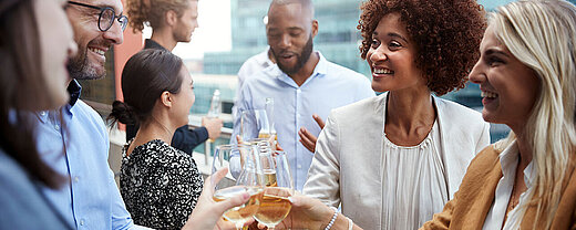 © Monkey Business - AdobeStock.com Kolleg:innen stoßen bei einem Business-Event mit Getränken an und genießen den gemeinsamen Austausch.