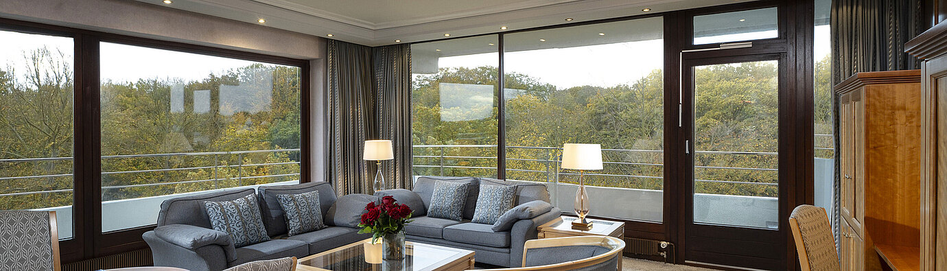 Wohnbereich der Grand Suite im Maritim Hotel Kiel mit großzügigen Fenstern, stilvoller Einrichtung und Blick ins Grüne.