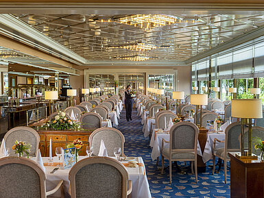 Großes, elegantes Restaurant mit langen, gedeckten Tischen, Kronleuchtern und Blumenarrangements für gehobenes Speisen.