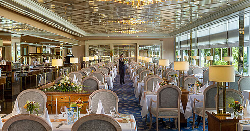 Großes, elegantes Restaurant mit langen, gedeckten Tischen, Kronleuchtern und Blumenarrangements für gehobenes Speisen.
