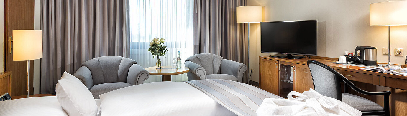 Superior Zimmer  Superior Doppelzimmer mit stilvoller Einrichtung, gemütlichem Sitzbereich, Wasserflaschen und einem Bademantel auf dem Bett.