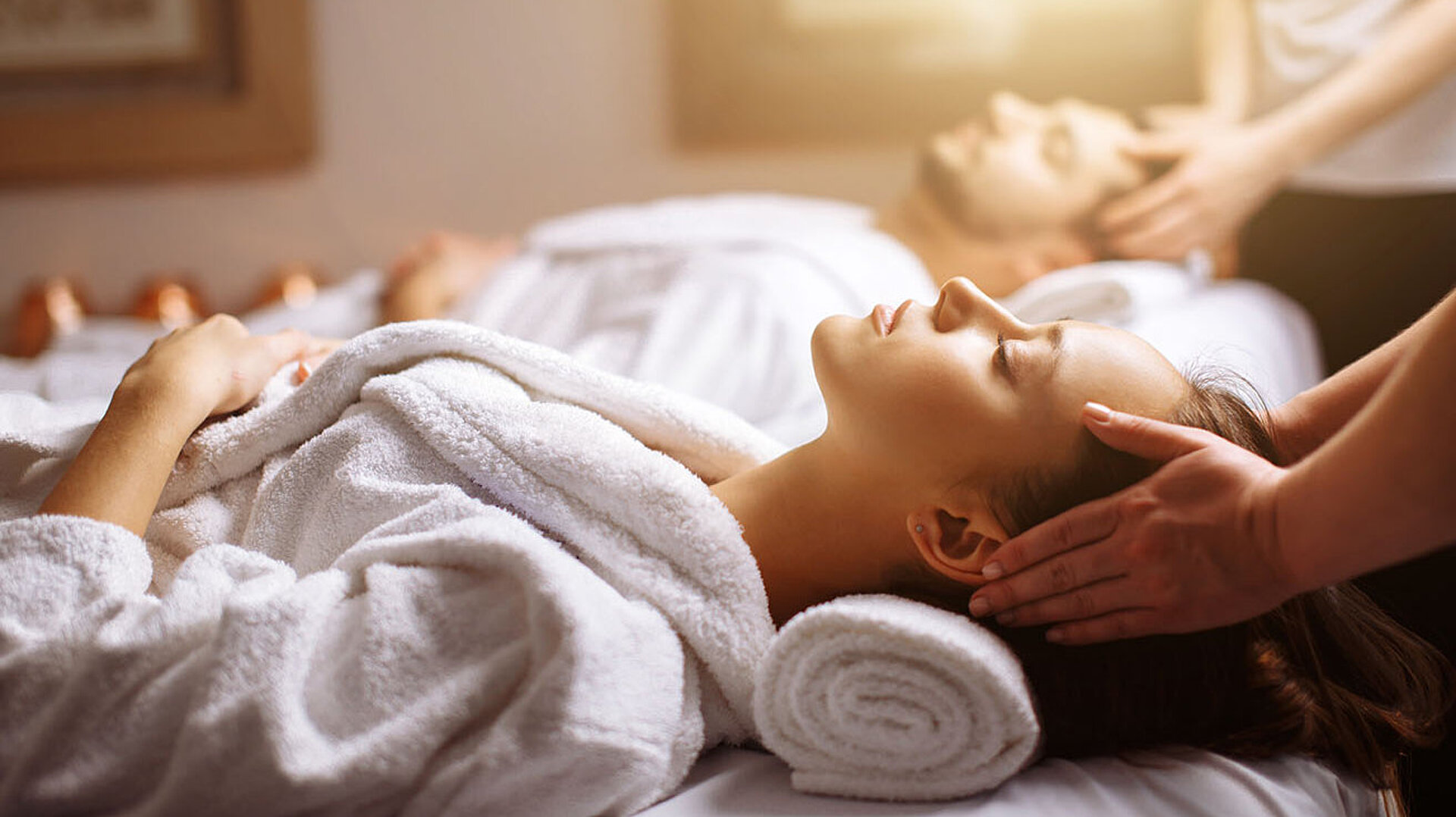 © alfa27 - AdobeStock.com Paar genießt entspannende Kopf- und Nackenmassage im Spa in weißen Bademänteln