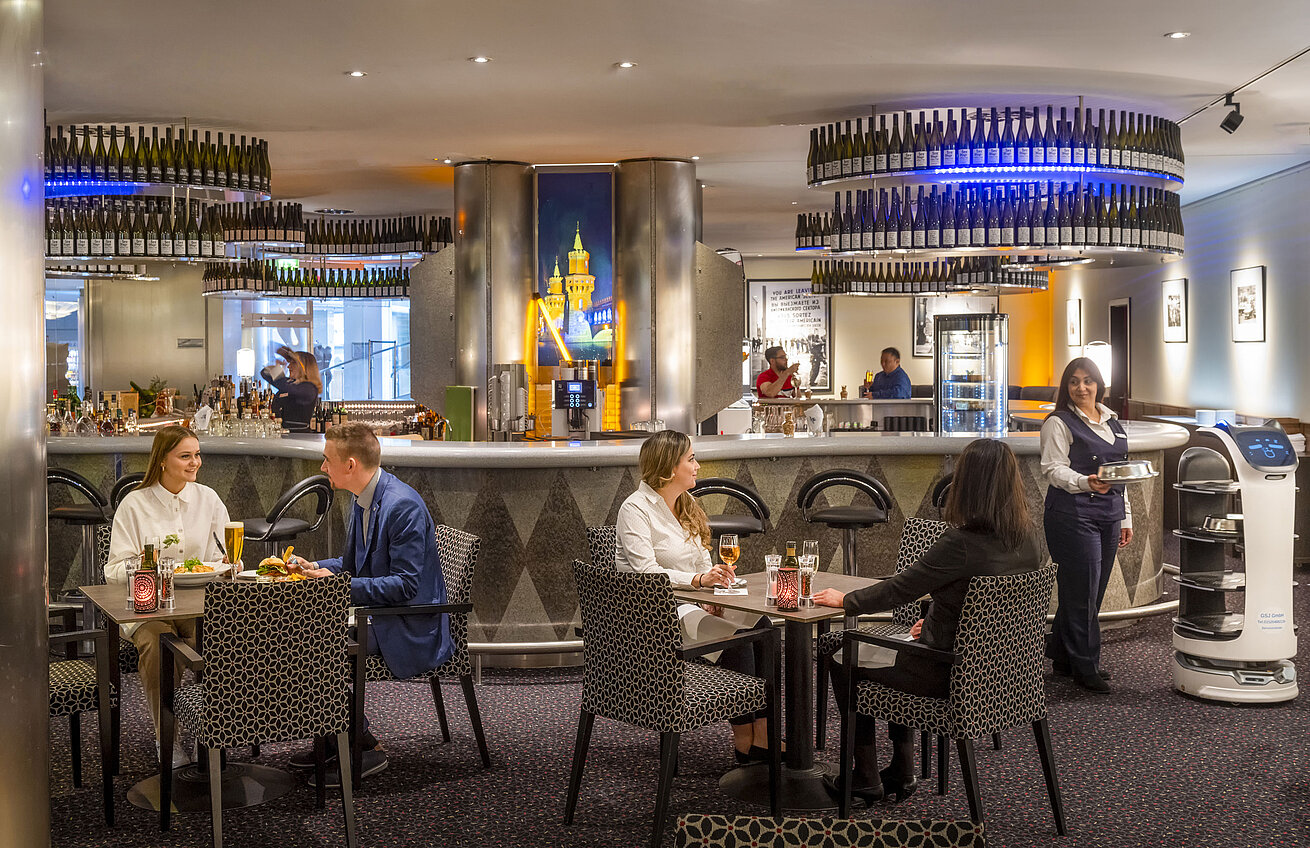 Restaurant & Bar Checkpoint Gäste speisen in der Bar des Maritim proArte Hotel Berlin, umgeben von modernen Einrichtungen und einem Serviceroboter.