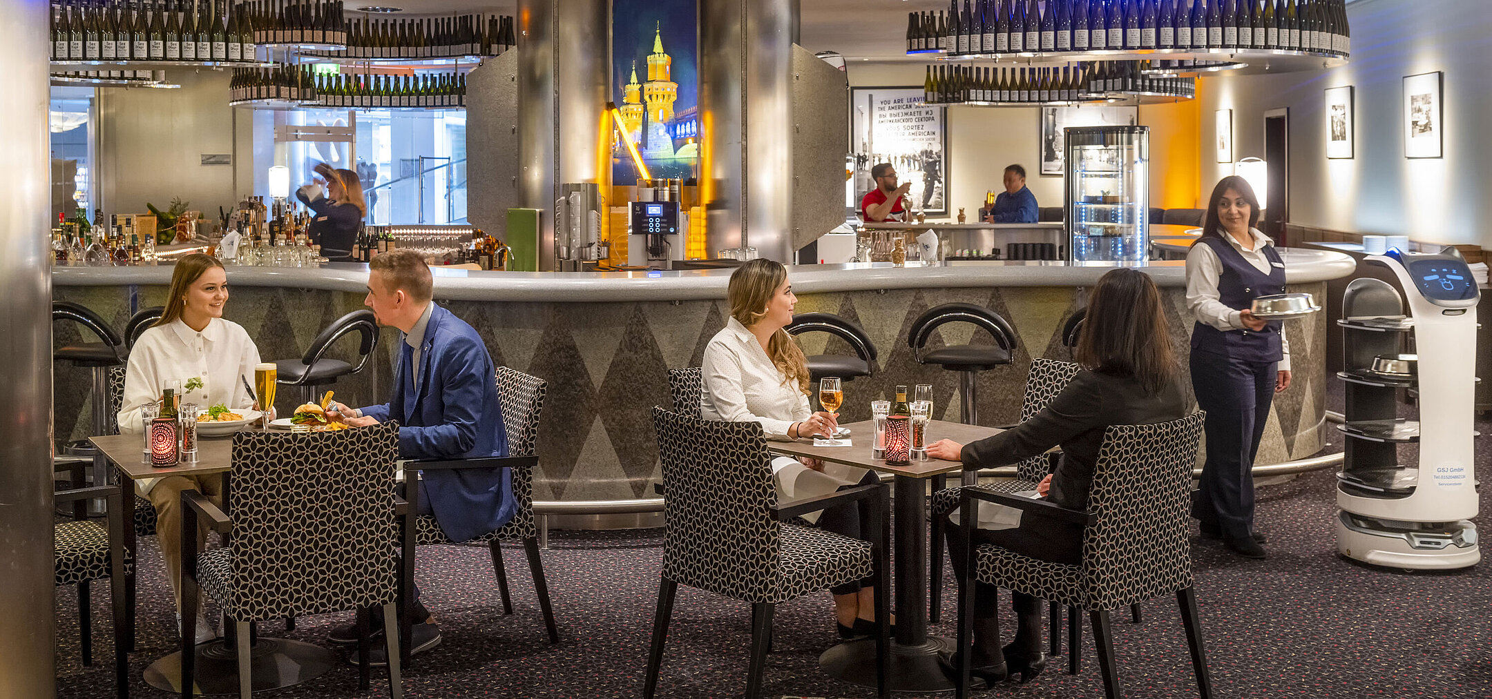 Gäste speisen in der Bar des Maritim proArte Hotel Berlin, umgeben von modernen Einrichtungen und einem Serviceroboter.