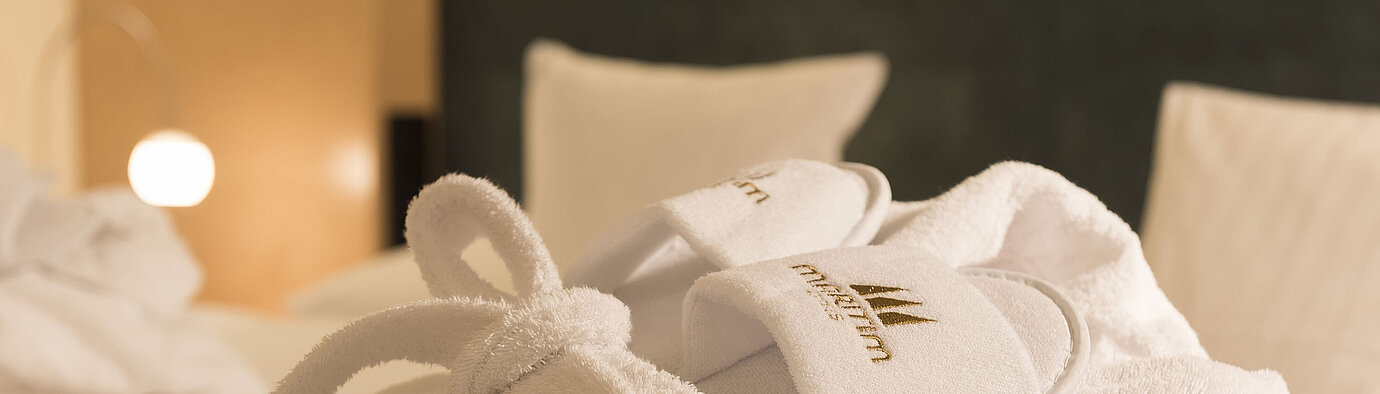 Bademantel  Ein flauschiger Bademantel und Hausschuhe mit Maritim-Logo auf einem Bett im Maritim proArte Hotel Berlin.