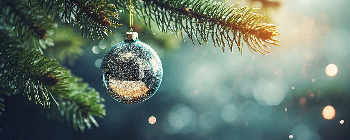 Christbaumkugel hängt an Tannenzweig mit weihnachtlicher Beleuchtung