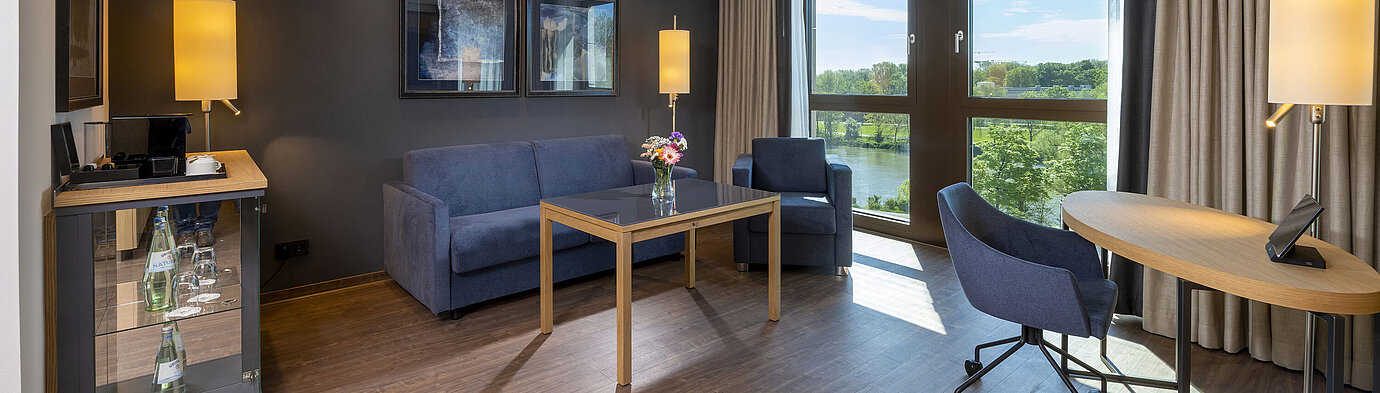 Helle Suite mit Sitzbereich, großem Fenster und Blick auf die Natur im Maritim Hotel Ingolstadt.