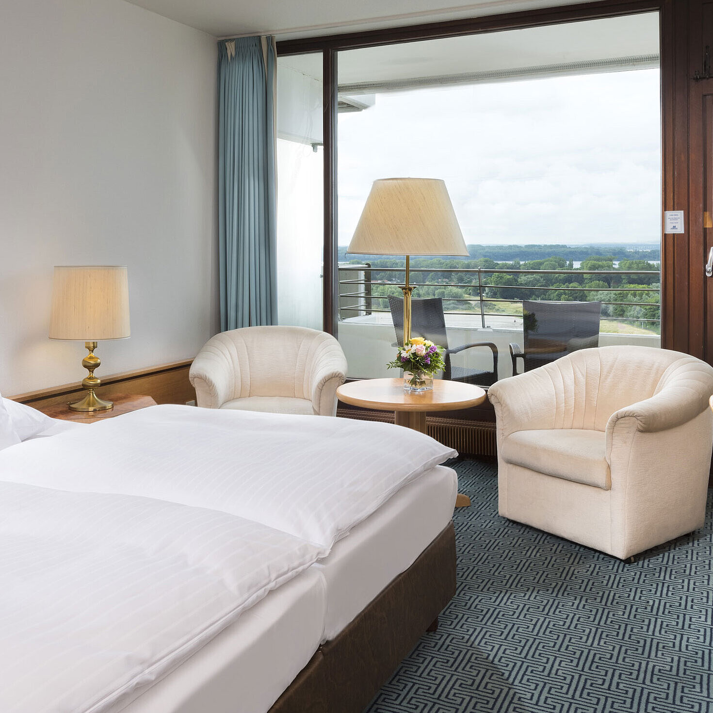 Doppelzimmer mit Sitzgruppe, Schreibtisch und Balkon mit Ausblick auf grüne Landschaft in Travemünde