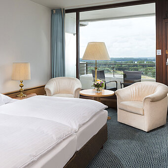 Doppelzimmer mit Sitzgruppe, Schreibtisch und Balkon mit Ausblick auf grüne Landschaft in Travemünde