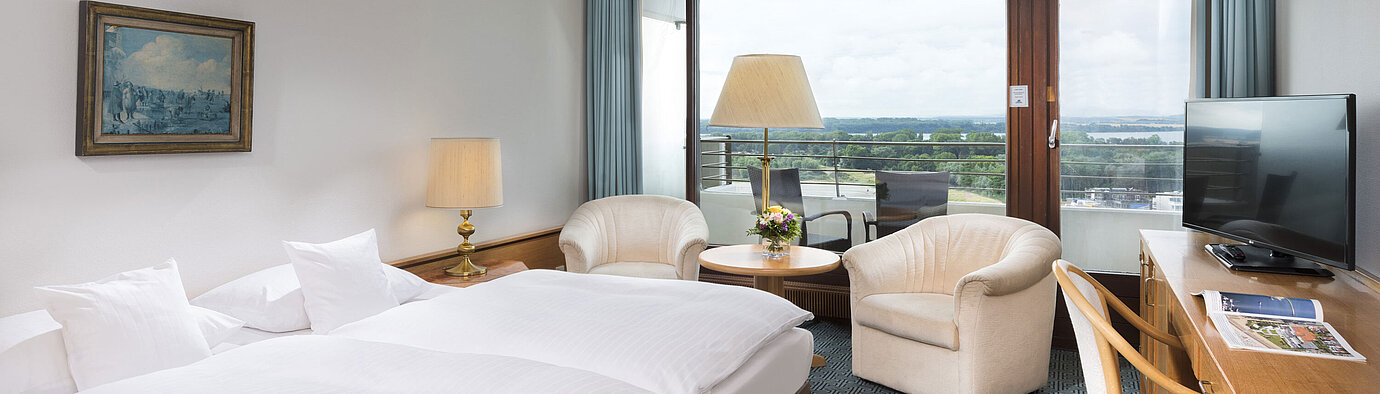 Doppelzimmer mit Sitzgruppe, Schreibtisch und Balkon mit Ausblick auf grüne Landschaft in Travemünde