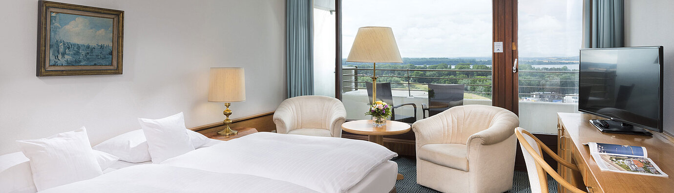 ComfortPlus Zimmer Doppelzimmer mit Sitzgruppe, Schreibtisch und Balkon mit Ausblick auf grüne Landschaft in Travemünde