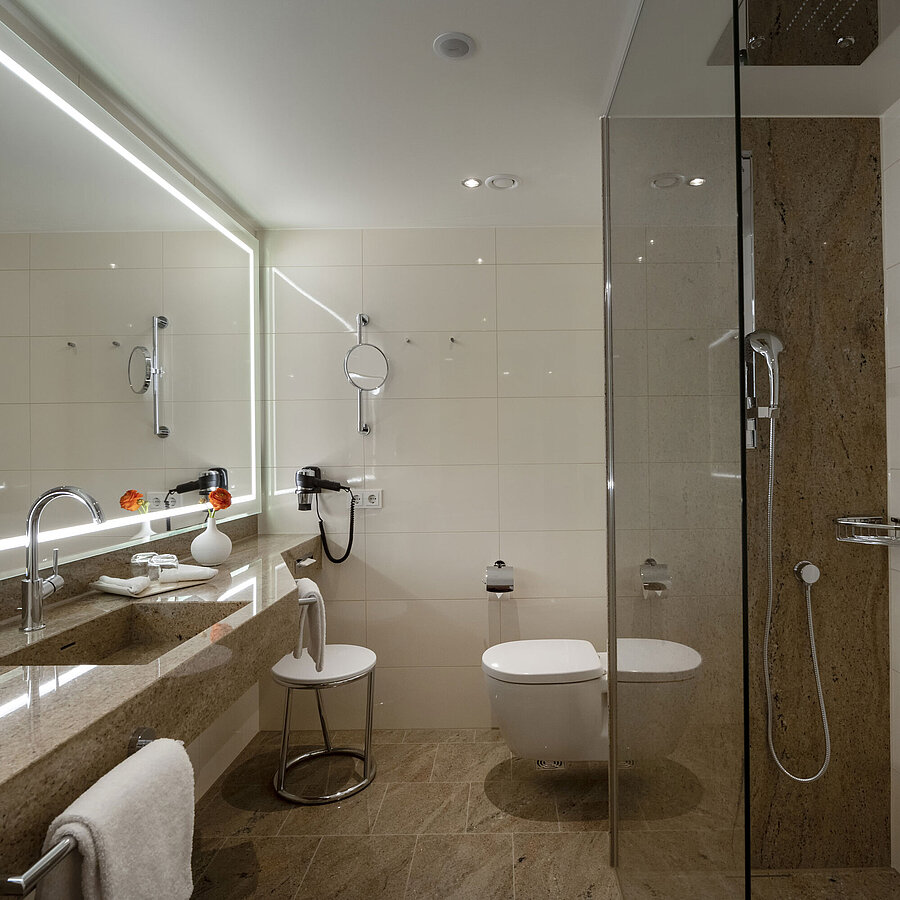 Badezimmer im Maritim Hotel Ingolstadt mit Glasdusche, großem Spiegel und stilvollem Design.