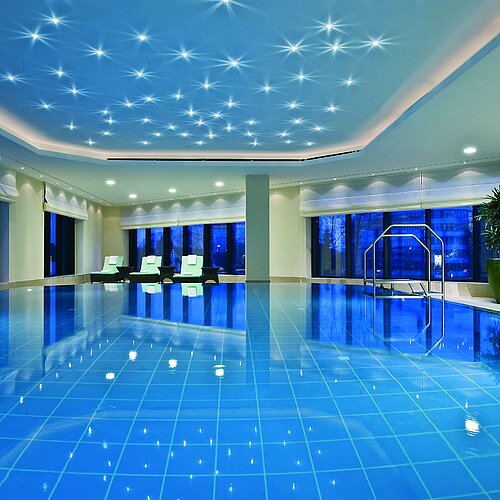 Beleuchteter Innenpool im Maritim Hotel Düsseldorf mit modernen Liegestühlen und Panoramafenstern, ideal für Erholung.