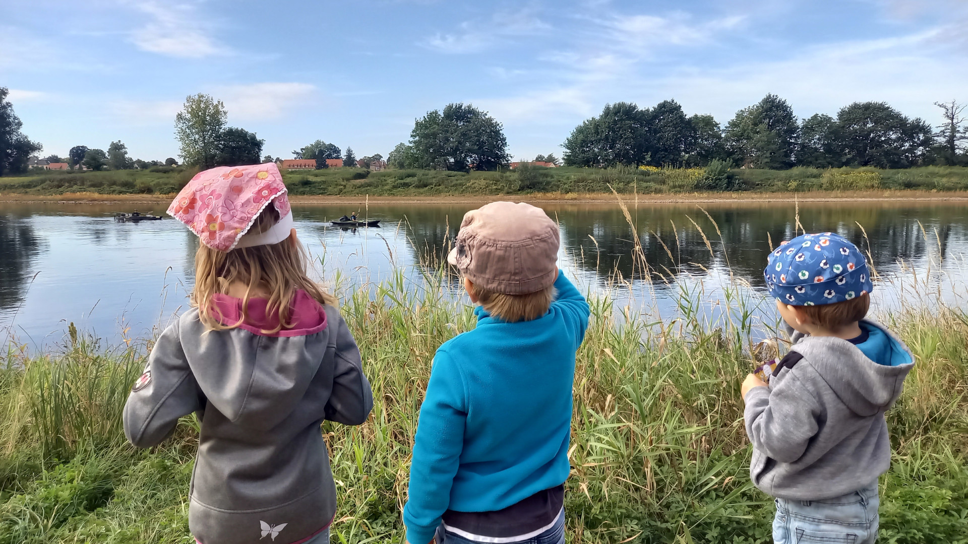 Ausflug an die Elbe Drei Kinder stehen am Uferrand und blicken auf die Elbe, wo zwei Personen in einem Kanu fahren.
