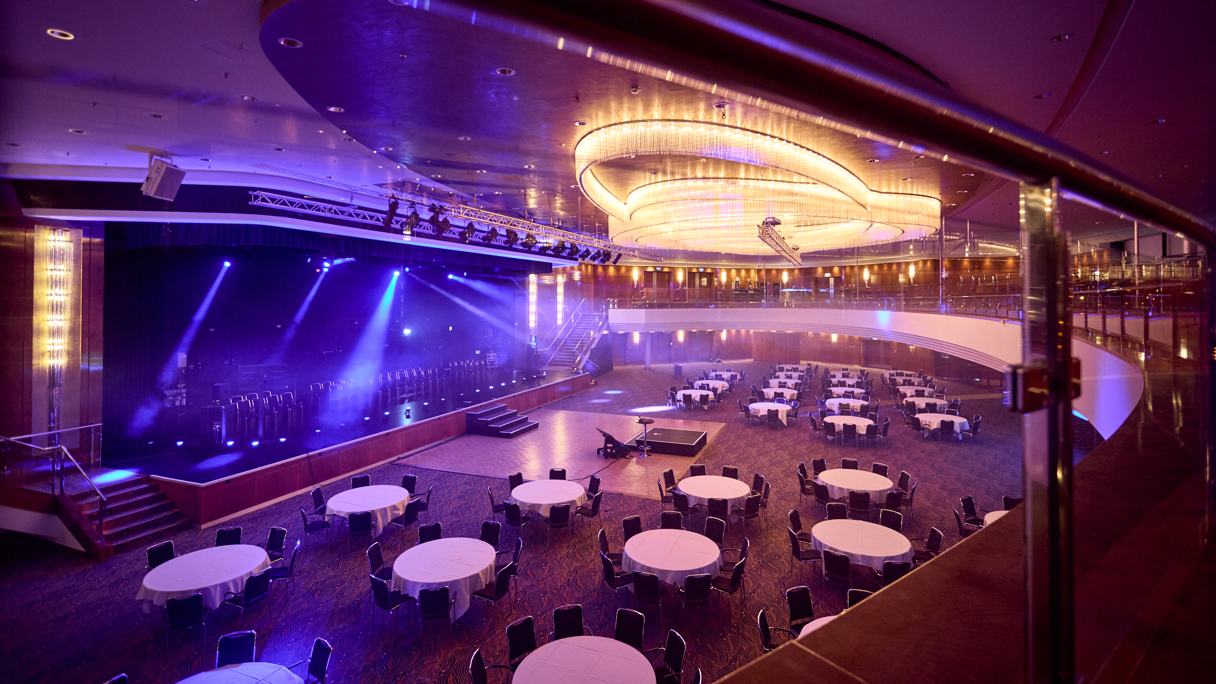 Moderner Ballsaal mit Bühne und Lichttechnik Großer Veranstaltungsraum mit Bühne, runden Tischen und atmosphärischer Beleuchtung für Events.