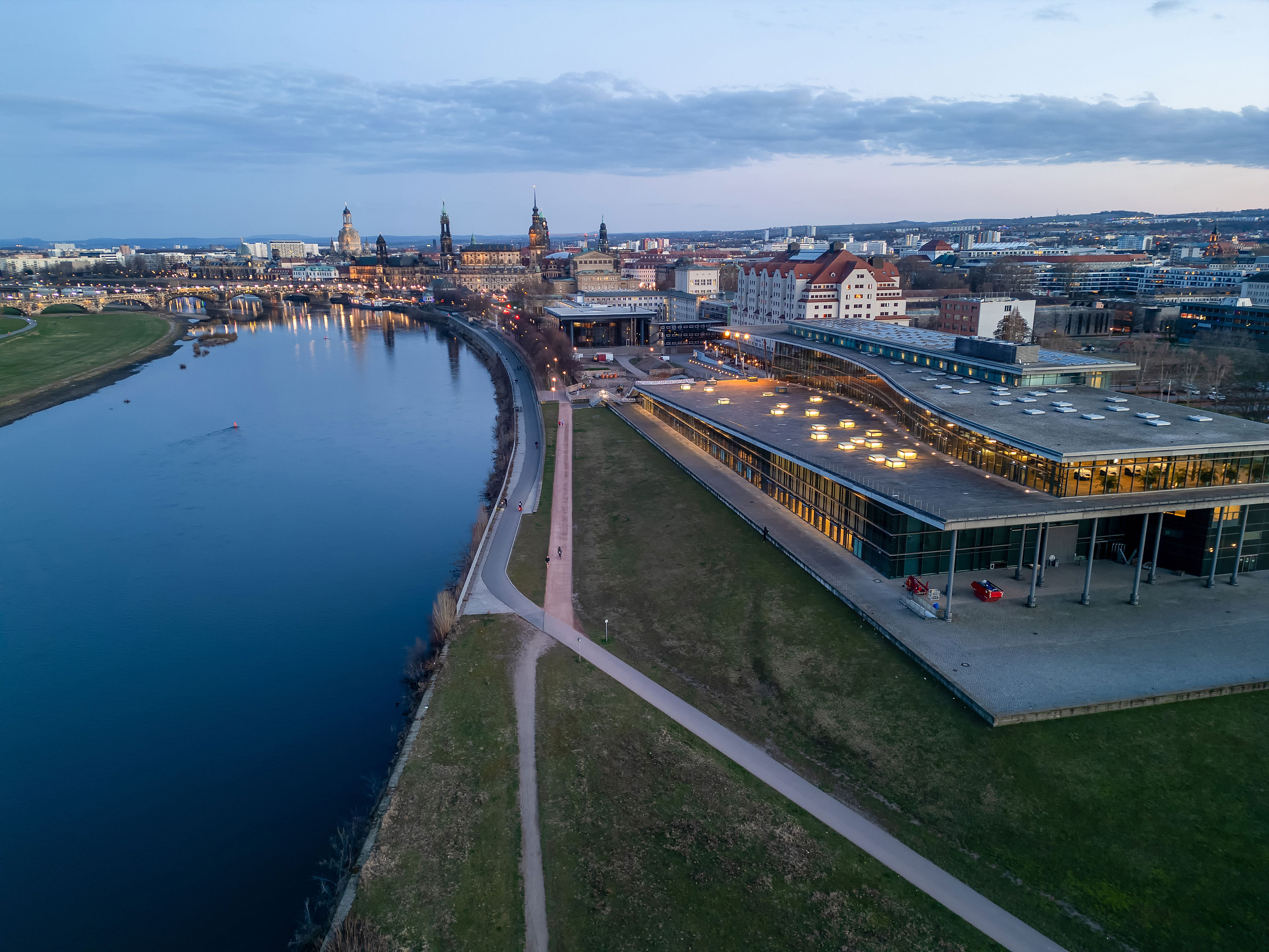 Außenansicht Luftaufnahme des Maritim Hotel Dresden an der Elbe mit Blick auf die Dresdner Altstadt bei Abenddämmerung.